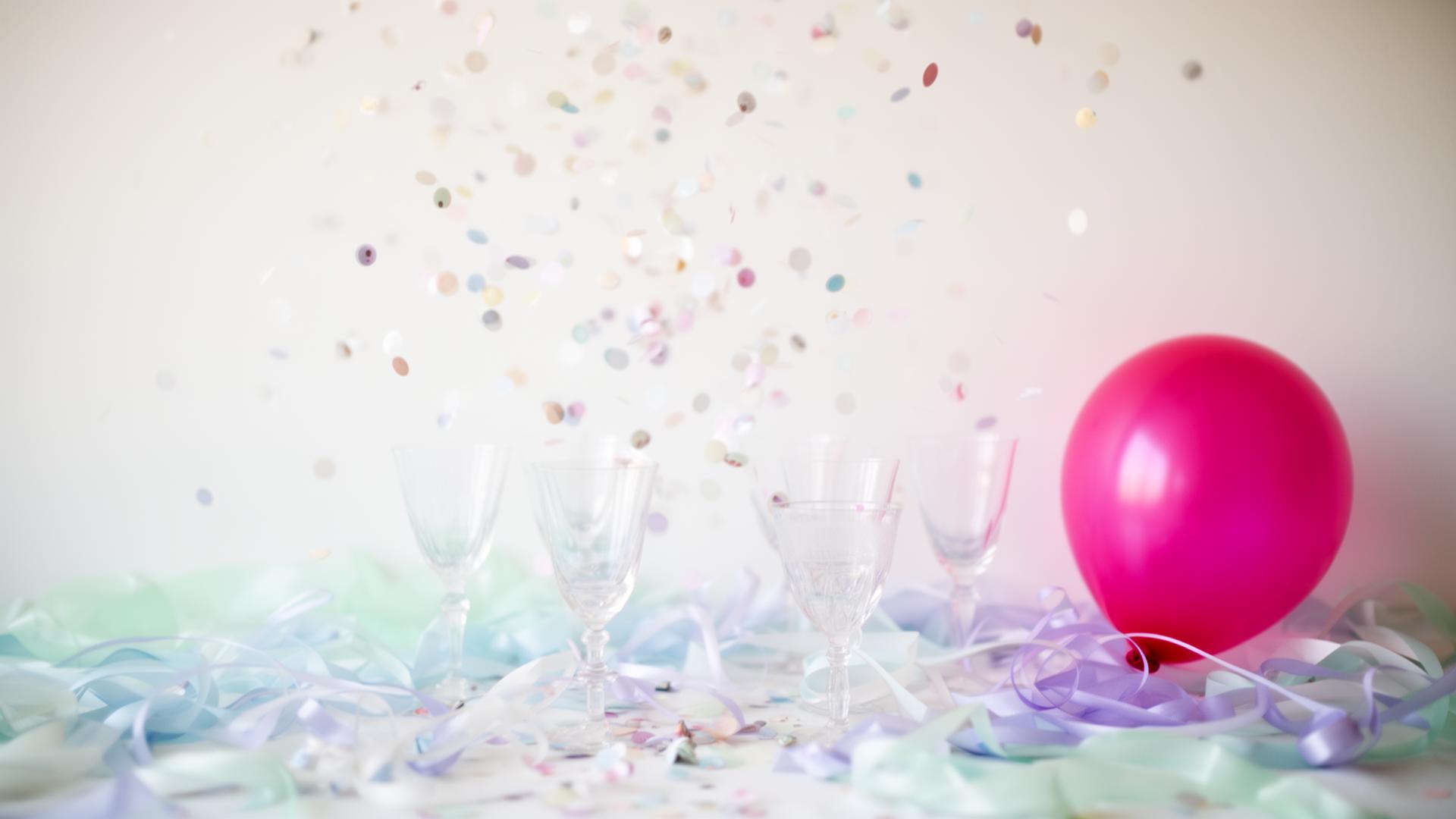 Pastel confetti and glassware celebrating with a fuchsia balloon
